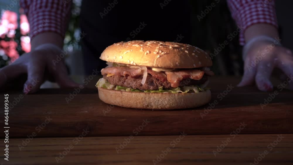 Street food. Hot fatty hamburger on a wooden board. Chef's hands in gloves and a baked burger in a cafe.