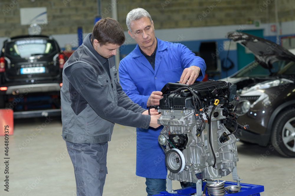 auto mechanic shows trainee maintenance of car engine
