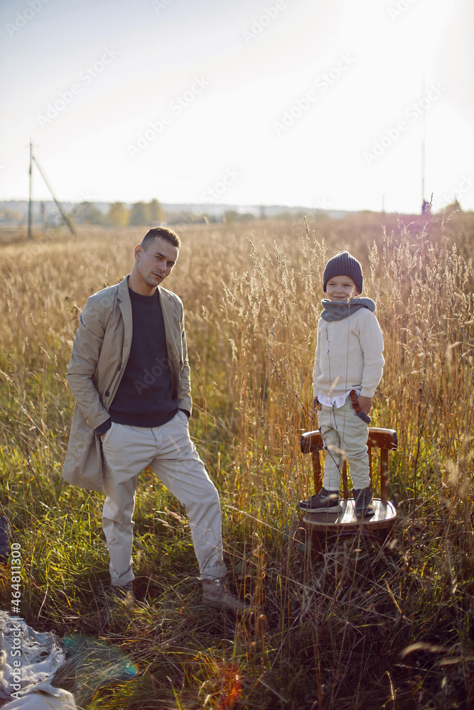 father and son are standing on a field with dry grass outside the city