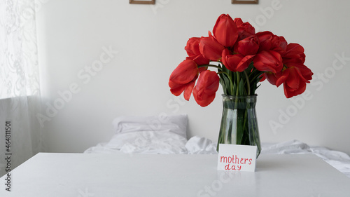 A bouquet of flowers in a vase for Mother's Day in the morning in the bedroom. Red tulips for Mom's holiday and Happy Mother's Day greeting card