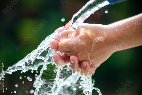 Close-up of a child's hands washing to remove germs. The green background of the outdoor garden.