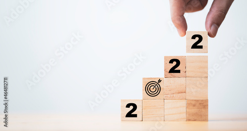 Hand holding 2022 and sign target board which print screen on wooden cube block stacking and copy space , Setup new business objective target in new year concept.