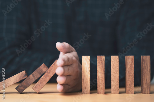 ฺBusinessman uses his hand to stop a falling wooden block to a standing wooden block domino , It is a symbol of protection against damage or stop loss for crisis management concept. photo