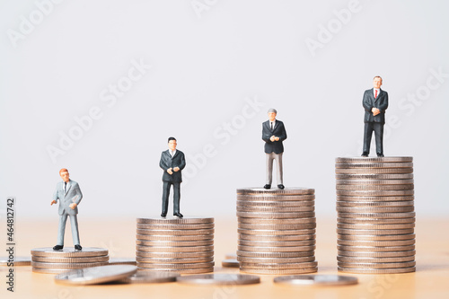 Different miniature businessman standing on different height coins stacking , Inequality income and salary in each position in company concept.