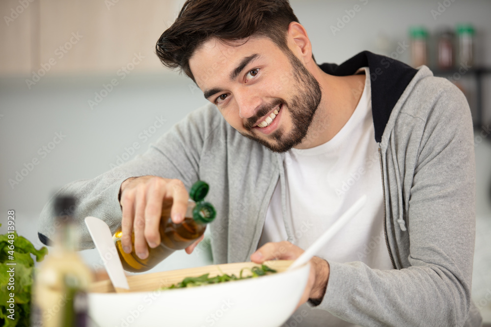 young man adding spice to the salad and smiling young man adding spice to the salad and smiling