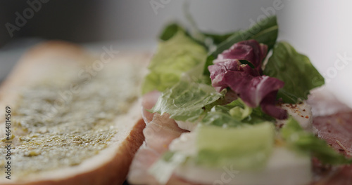 greens on mozzarella slices on prosciutto slices on baguette to make sandwich