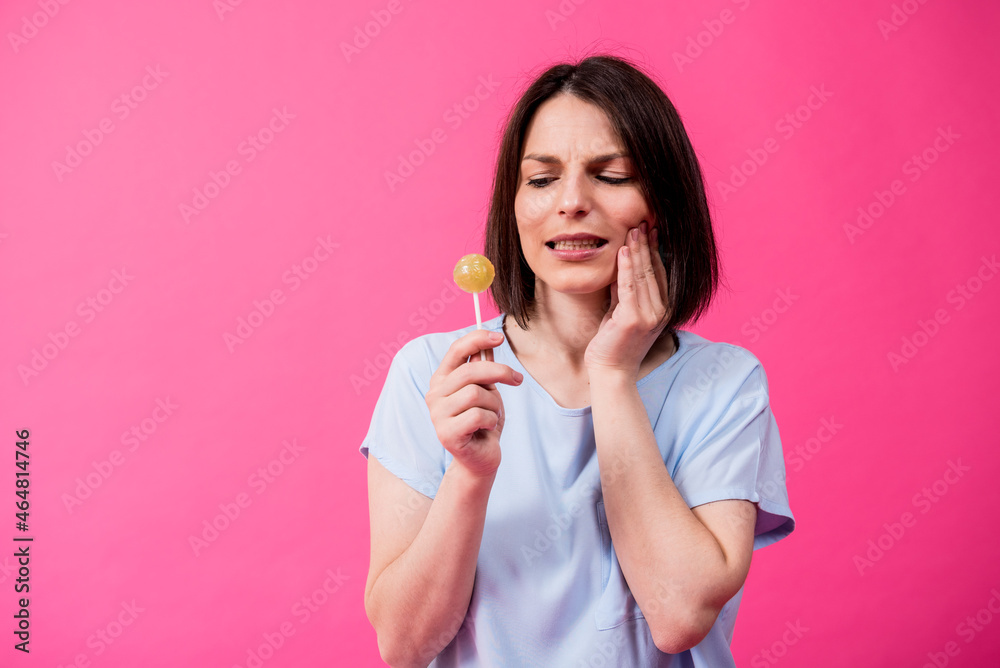 Young woman with sensitive teeth eating sweet lollipop on color background Young woman with sensitive teeth eating sweet lollipop on color background