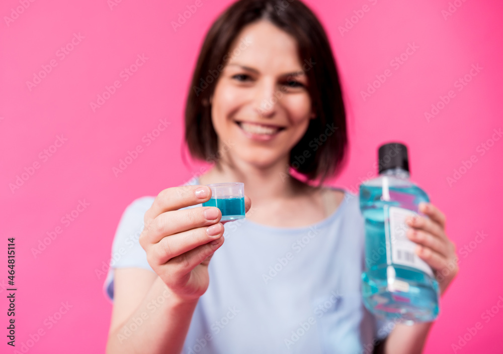 Beautiful girl uses mouthwash on the pink background Beautiful girl uses mouthwash on the pink background