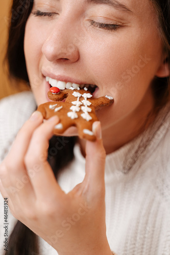 Young appetizing woman takes a bite of traditional christmas gingerbread cookie. Concept of sweet pastries and healthy teeth.