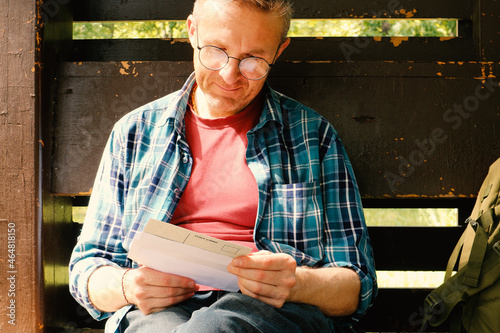 Billede på lærred A young man in glasses and a shirt is reading a letter while sitting in the park in the gazebo
