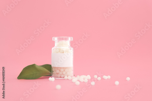 Close-up image of homeopathic globules in glass bottle on pastel pink background. Homeopathy pharmacy, herbal, natural medicine, alternative homeopathy medicine, healthcare. Free space, copy space.