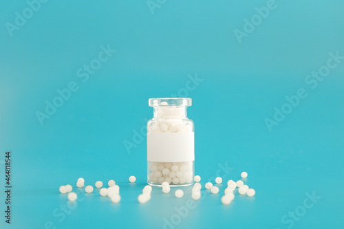 Close-up image of homeopathic globules in glass bottle on blue background. Homeopathy pharmacy, herbal, natural medicine, alternative homeopathy medicine, healthcare. Free space, copy space.