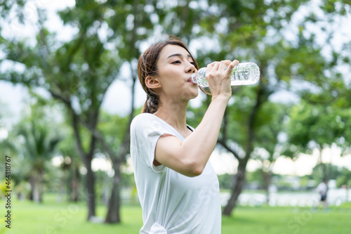 Asian young girl athlete drink bottle of water after exercise in park. 