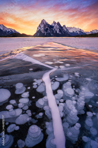 Stunning sunrise with leading ice creacked line and trapped frozen methane bubbles within ice surface, Lake Abraham, Alberta. Winter storm in Canada. photo