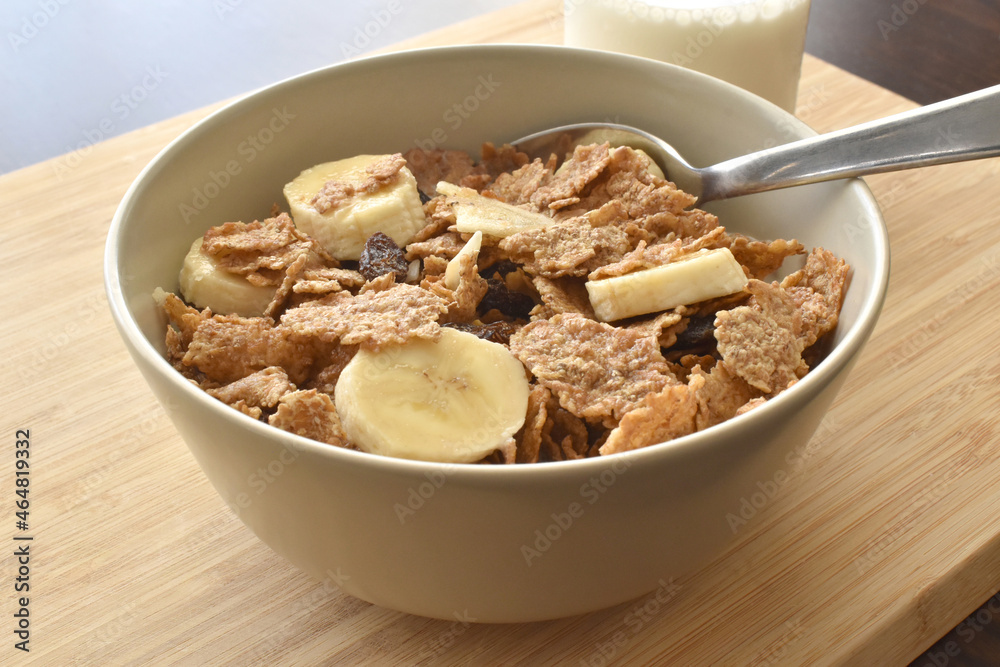 Fruit and fiber cereal with banana and milk with a spoon in a bowl on a bamboo chopping board. Fruit and fiber cereal with banana and milk with a spoon in a bowl on a bamboo chopping board.