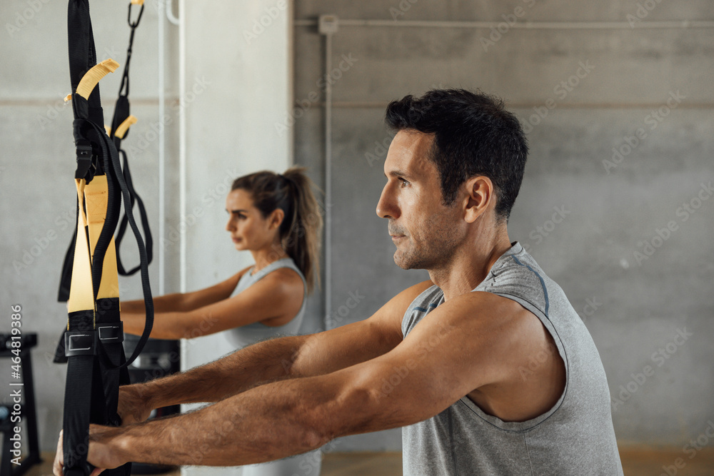 Fit man and woman train legs and abs with suspension straps at gym club.