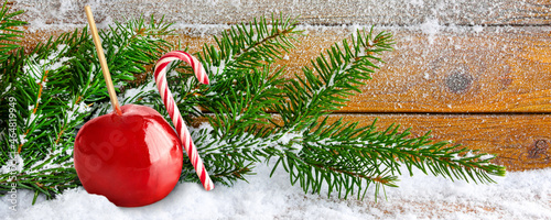 Christmas time red candied apple and candy cane with fir branches and snow on wooden background photo