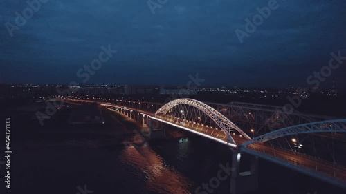 A motorcade of three cars rides over a bridge over a river at night photo
