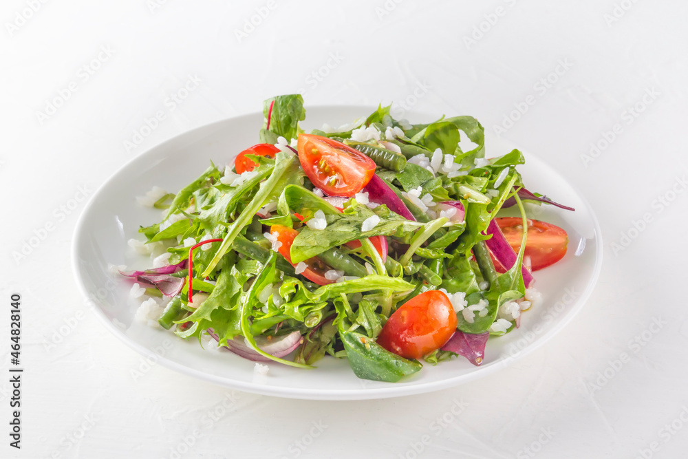 Greens, tomato and rice salad with arugula, green peas and red onions. Close-up
