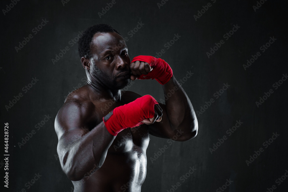 Athletic boxer during boxing training. Fitness african american muscular model over black background. Strength, fighting and motion project.