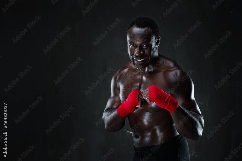 African american athletic fighter demonstrating boxing stance, raising fists up, black background, copy space