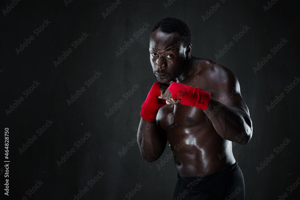 Athletic boxer during boxing training. Fitness african american muscular model over black background. Strength, fighting and motion project.