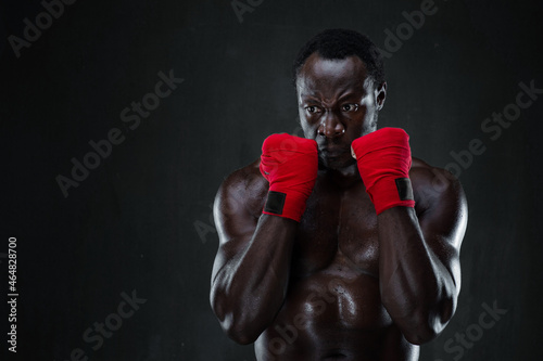 Athletic boxer in boxing protective rack. Portrait of african american male fit model over black background. Life, sport, fighting and protection project.