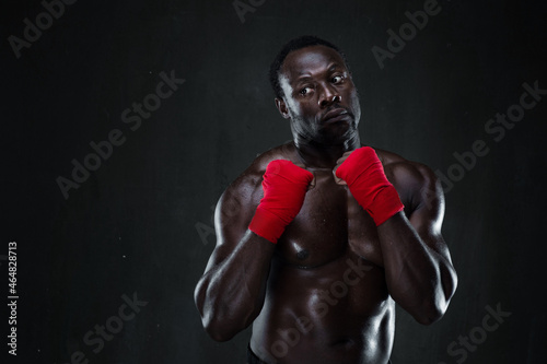 Athletic boxer in boxing protective rack. Portrait of african american male fit model over black background. Life, sport, fighting and protection project. © Admiral