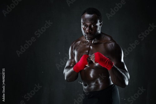 African american athletic fighter demonstrating boxing stance, raising fists up, black background, copy space © Admiral