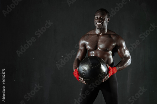 African american boxer fighter holding fitness wall ball in hands, black background. Strong man with soft medicine ball after cross training workout. Copy space.