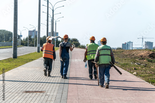 A team of workers in helmets and overalls with shovels go to the place of work. Work in an urban environment.