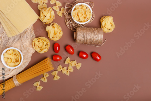 Yummy italian pasta and cherry tomatoes in rustic style on brown background. Traditional italian cuisine top view. Pasta is the traditional italian food. Spaghetti, fettuccine, farfalle flat lay view.