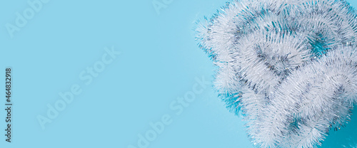 White fluffy Christmas New Year tinsel on a blue background. Top view, flat lay. Banner photo