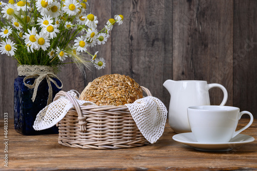 Homemade bread, cup, milk jug and bouquet of daisies on wooden table