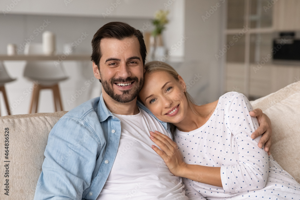 Portrait of affectionate bonding young married couple relaxing on comfortable sofa at home. Joyful sincere loving millennial family spouses looking at camera, spending time together on weekend. Portrait of affectionate bonding young married couple relaxing on comfortable sofa at home. Joyful sincere loving millennial family spouses looking at camera, spending time together on weekend.