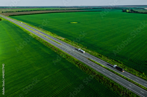 two fuel tanker trucks shipping fuel on the countryside road along the green fields at sunset. seen from the air. Aerial view landscape. drone photography. cargo delivery