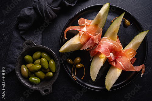 Jamon serrano, ham or prosciutto with melon and olives, a traditional Spanish and Italian appetizer on plate, top view