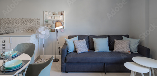 Modern interior of living room in studio apartment. Grey tones. Lamp near cozy couch with cushions. Dinner table. photo