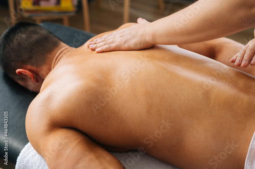 Close-up top view of unrecognizable male masseur massaging back of muscular sportsman lying on massage table. Professional therapist making movements with strong arms along the spine toward head.