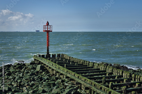 Horizontal view on a red seamark standing on breakwaters at the coast of the North sea in summer during ebb on a sunny day. Copy space