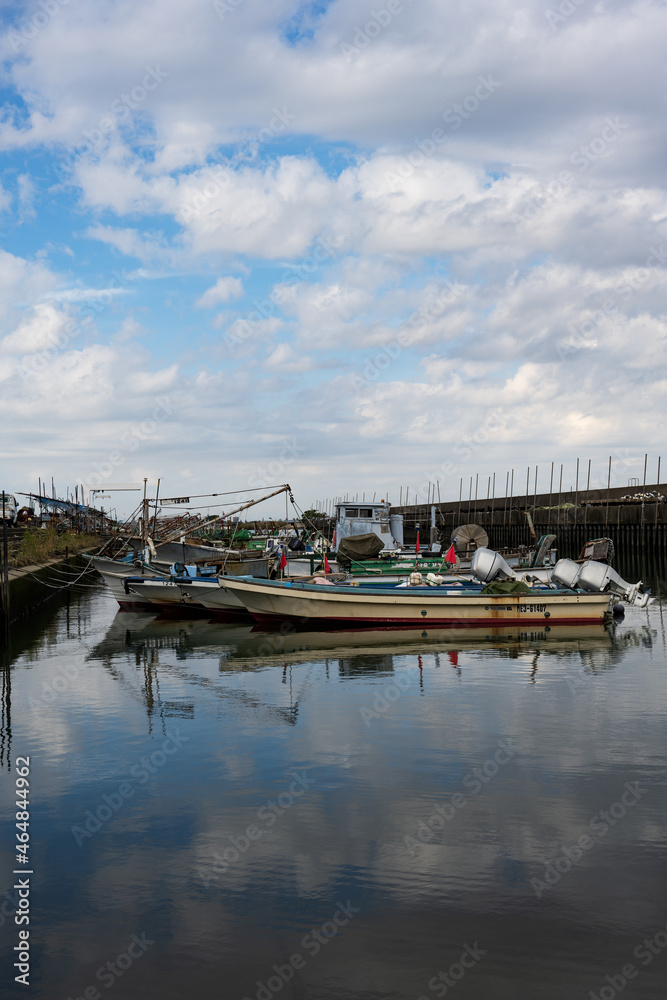 小さな漁港に停泊する小型の漁船が青い空を写す波間に漂う

