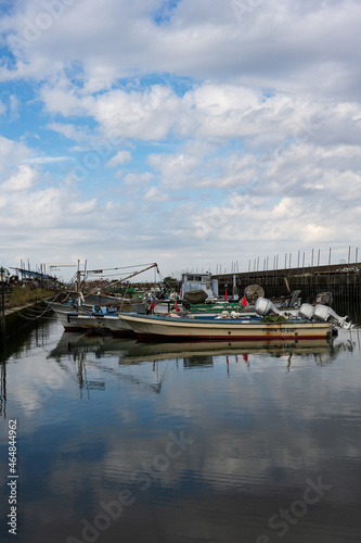 小さな漁港に停泊する小型の漁船が青い空を写す波間に漂う  © Mthrmyt