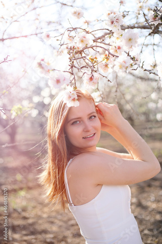 Portrait of a young blonde girl in a blooming spring garden. Almond trees are blooming
