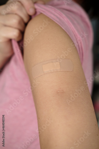 Hand after being vaccine against covid-19. Woman lifts the sleeve of a t-shirt and shows her shoulder with a bandage after vaccination.