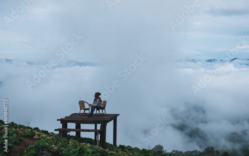 A young female traveler sitting on wooden balcony with a beautiful nature views and sea of fog