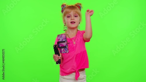 Happy funky young female blogger child kid girl, recording funny dancing video on smartphone for social network or personal channel, having fun entertaining on weekend at home on chroma key background