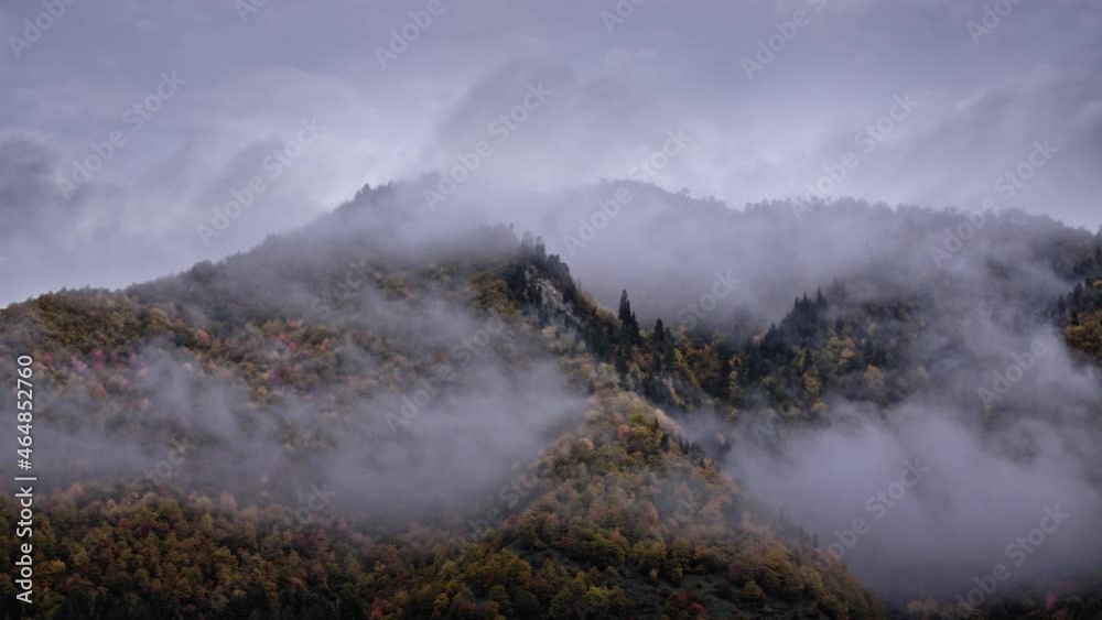 Timelapse of beautiful misty mountains peaks in autumn, golden and red foliage trees.