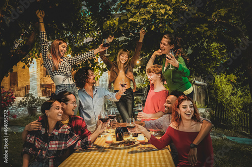 Canvas Print Multiracial friends enjoying dinner and drinking red wine in the garden - People having fun after dinner in the courtyard of the restaurant, girls dancing and people toasting - Friendship concept