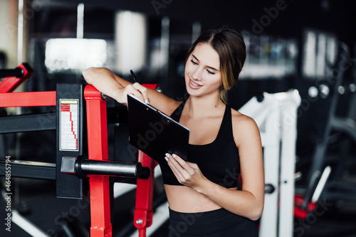 Modern personal trainer girl in modern gym with workout plan in hand
