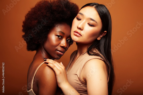 young pretty asian, afro woman posing cheerful together on brown background, lifestyle diverse nationality people concept